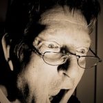 口を開けているメガネをかけた男性の白黒写真