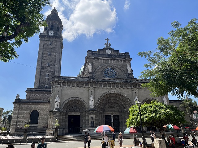 教会の尖塔のある建物、背景はManila Cathedral